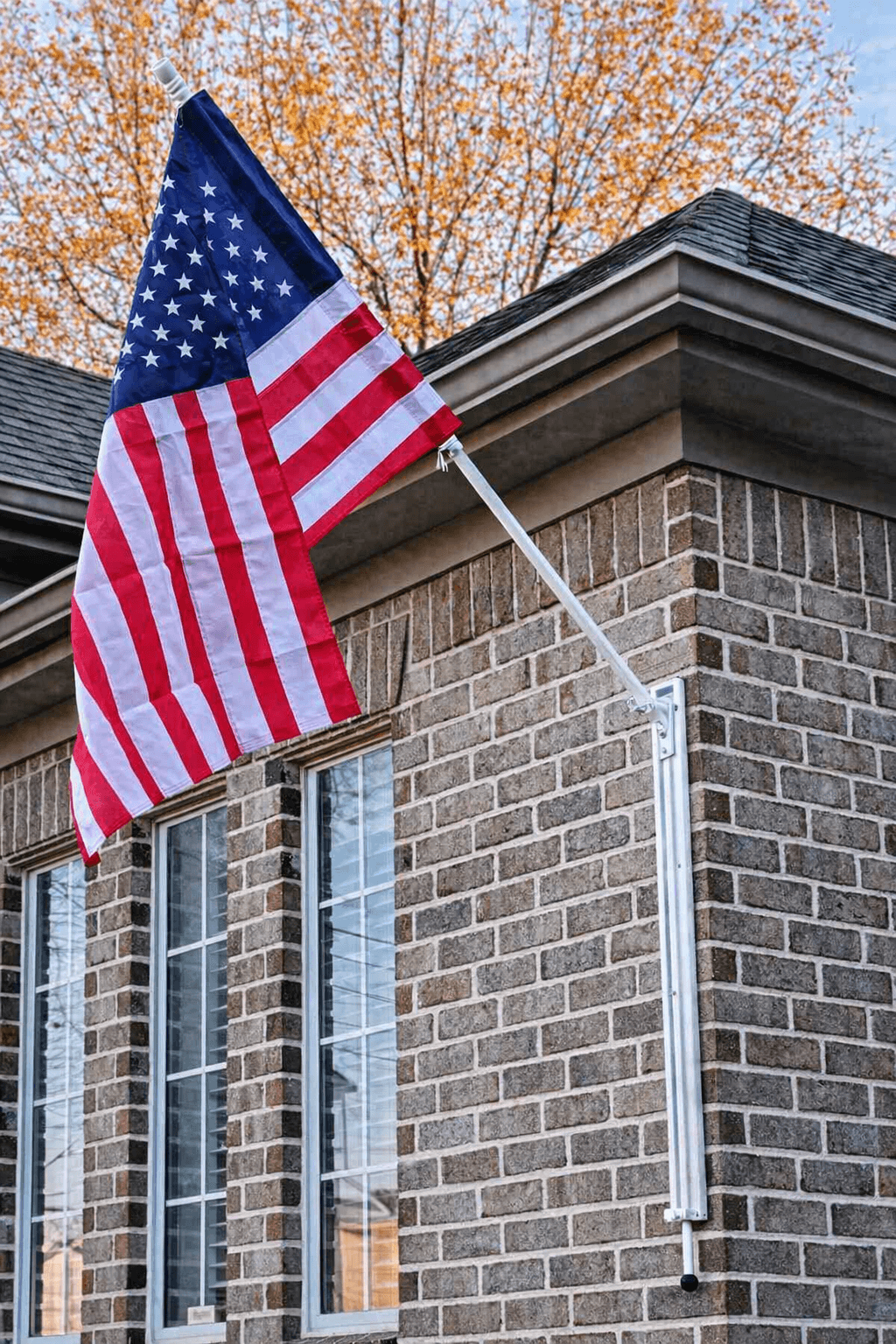 White VersaMAST System with American flag in raised angled display position on brick home